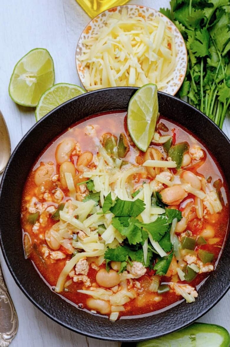 white bean turkey chili in a black bowl with sliced limes and cheese and cilantro. 