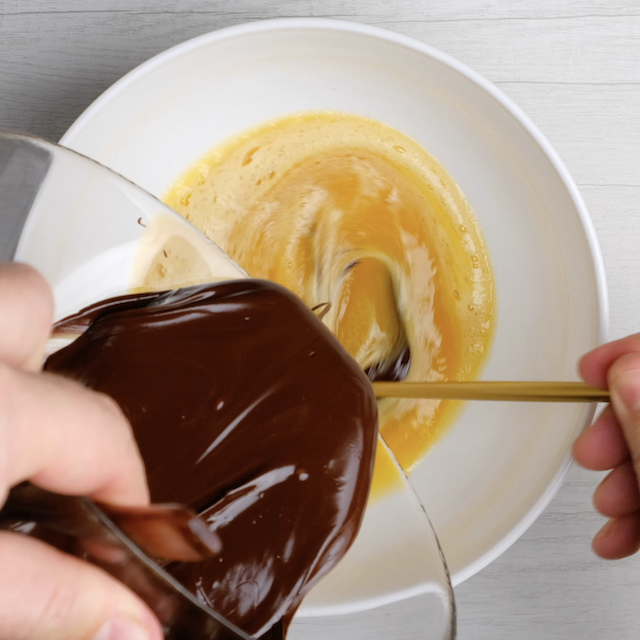 Melted chocolate mixture being whisked into egg mixture ot make chewy brownie cookies.