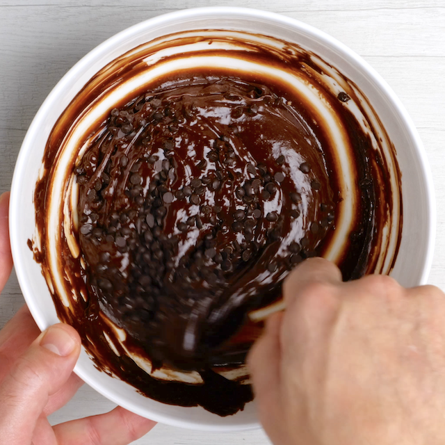 Mini chocolate chips being stirred into brownie cookie batter.