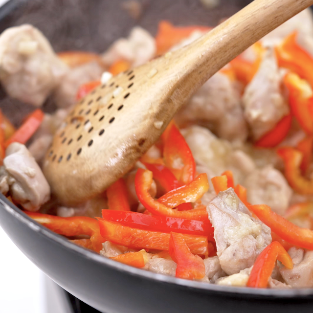 Bell peppers being cooked in a pan with chicken to make Thai basil chicken.
