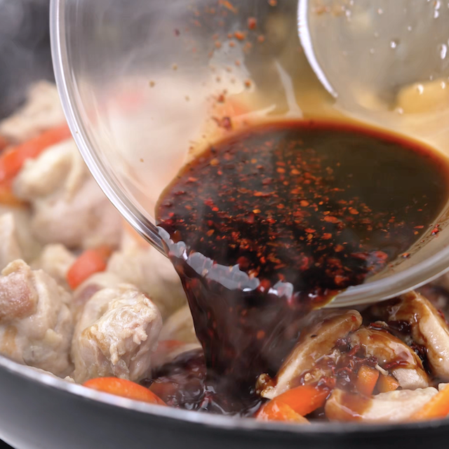 Sauce being poured into a pan to make Thai basil chicken.