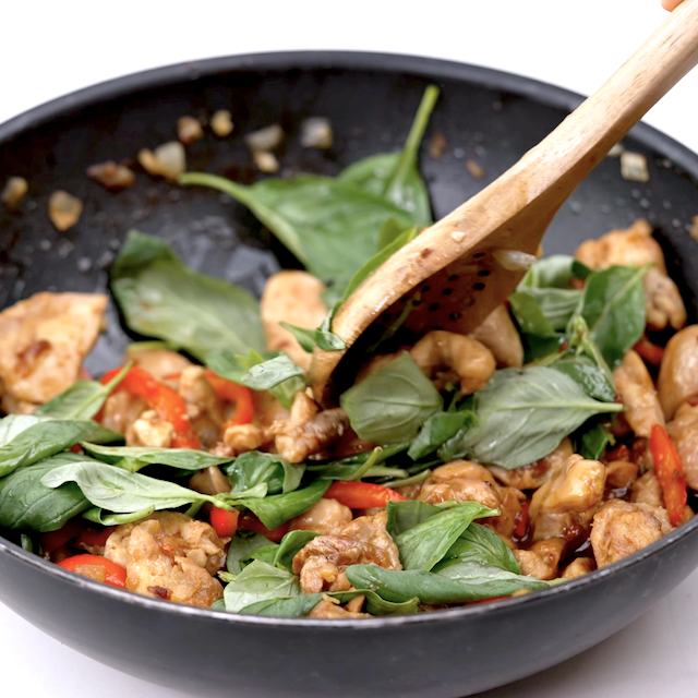 Thai basil leaves being folded into stir fry to make thai basil chicken.