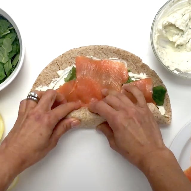Smoked salmon pinwheels tortillas being rolled to create a log to refrigerate.