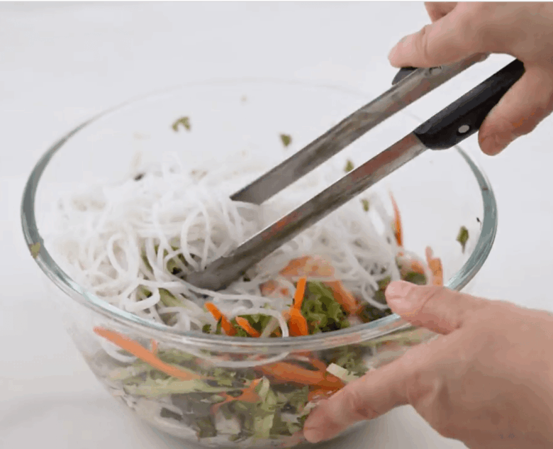 Virtų ryžių makaronų pridėjimas prie kitų „Spring Roll Bowl“ ingredientų.