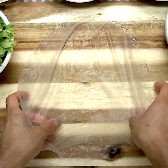 A soaked rice wrapper being laid down on a chopping board.