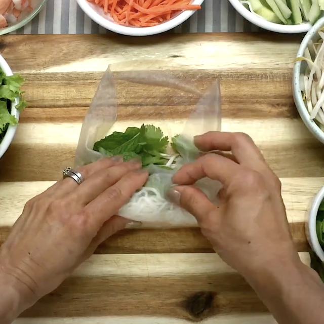 A Vietnamese spring roll being rolled on clean, flat surface.