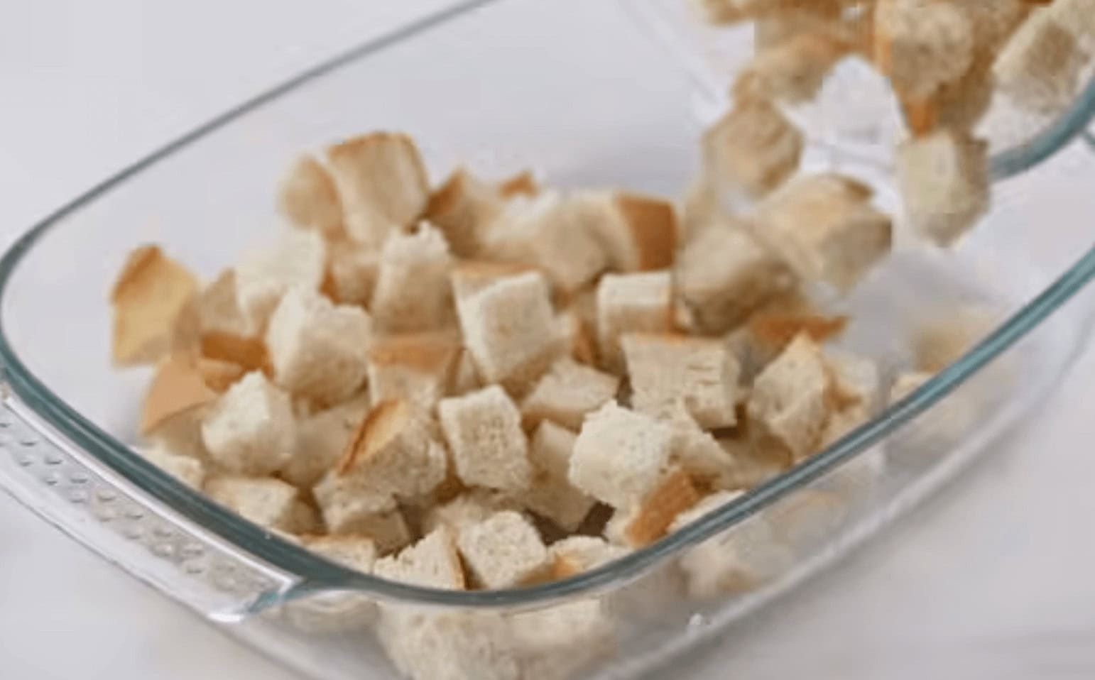 Adding the diced bread to the prepared casserole dish.