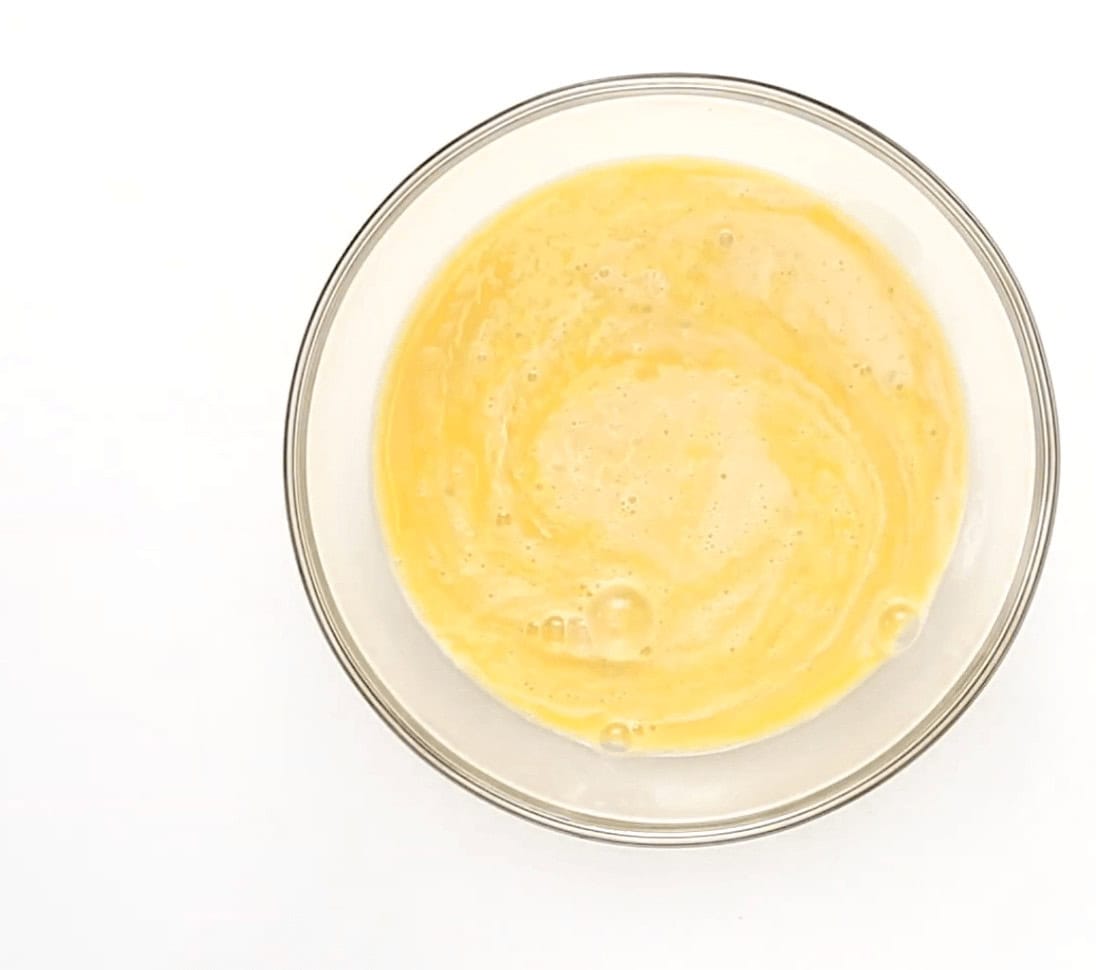 Whisking the egg mixture in a clear glass bowl.