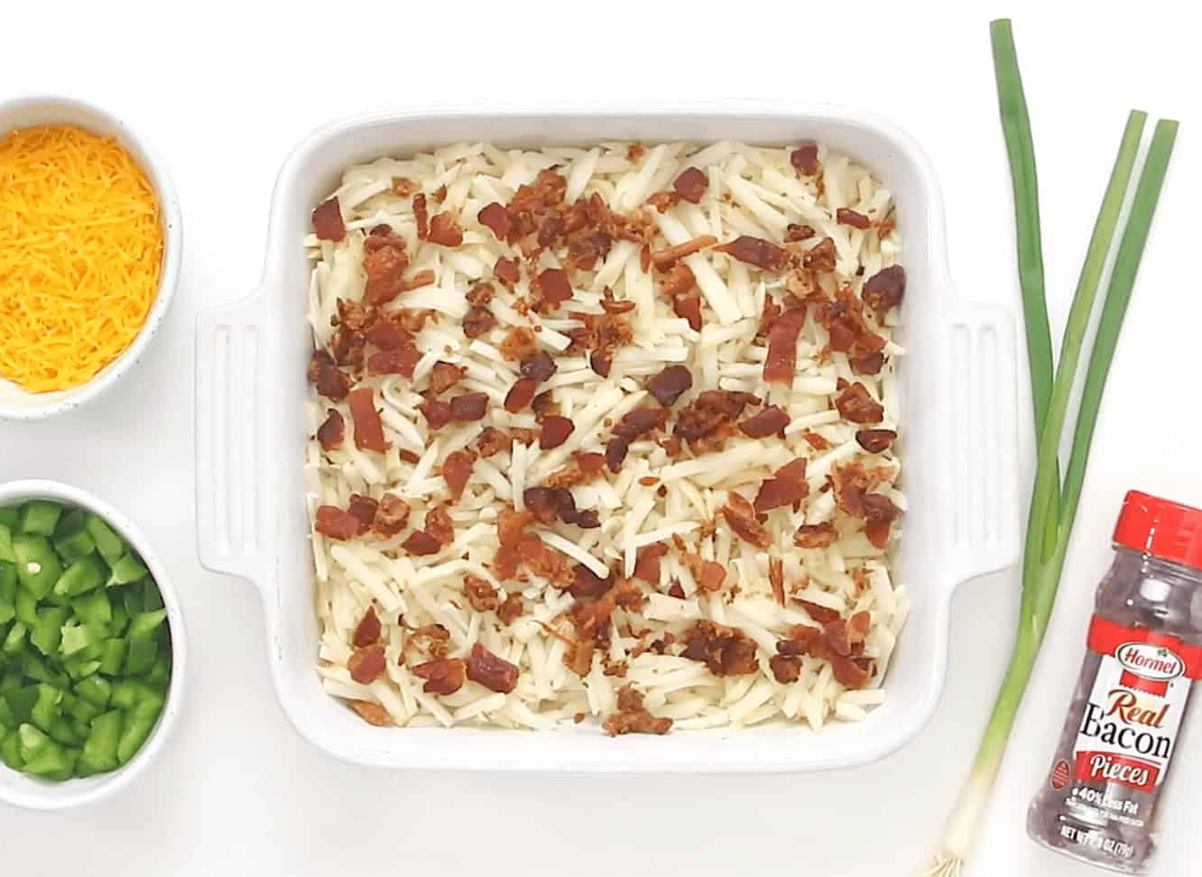 Adding the hash browns and bacon to a white casserole dish.