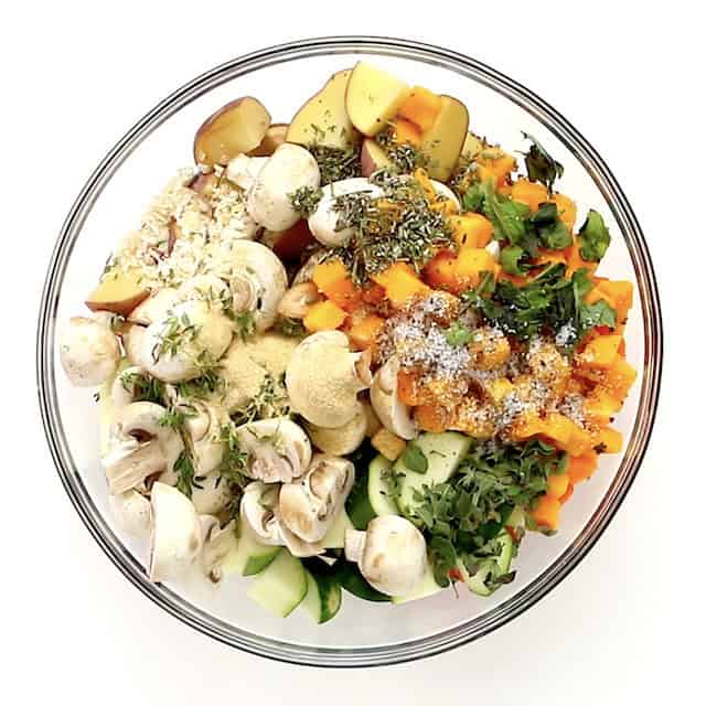Fresh herbs and seasonings added over chopped veggies in a glass bowl to make easy roasted vegetables.