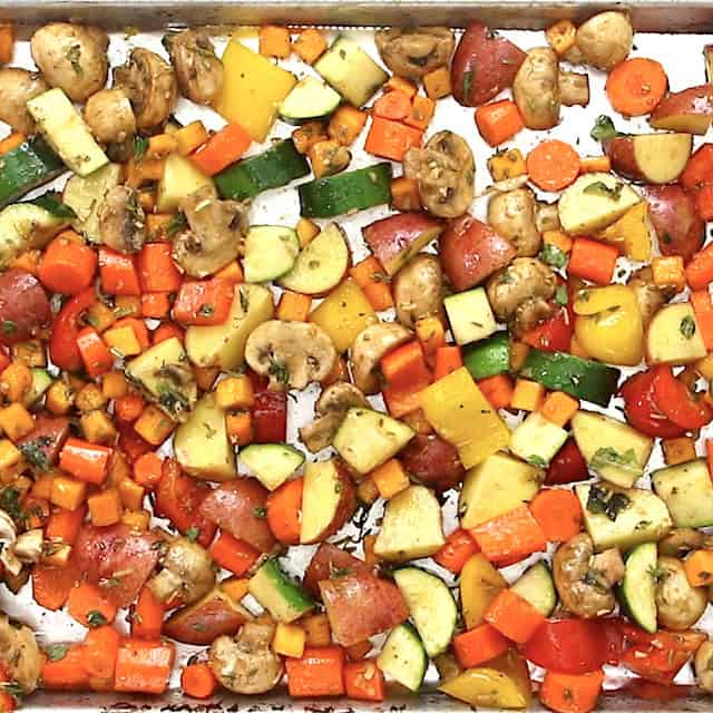 Chopped and seasoned vegetables spread on a baking sheet, ready to be roasted to make easy roasted vegetables.