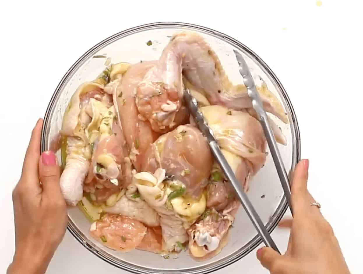 Pouring the seasoning mixture over the top of the chicken in a glass bowl and tossing with tongs.