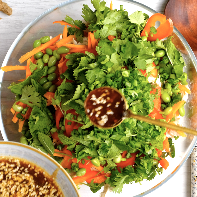 Dressing being added to Vietnamese chicken salad veggies, ready to toss.