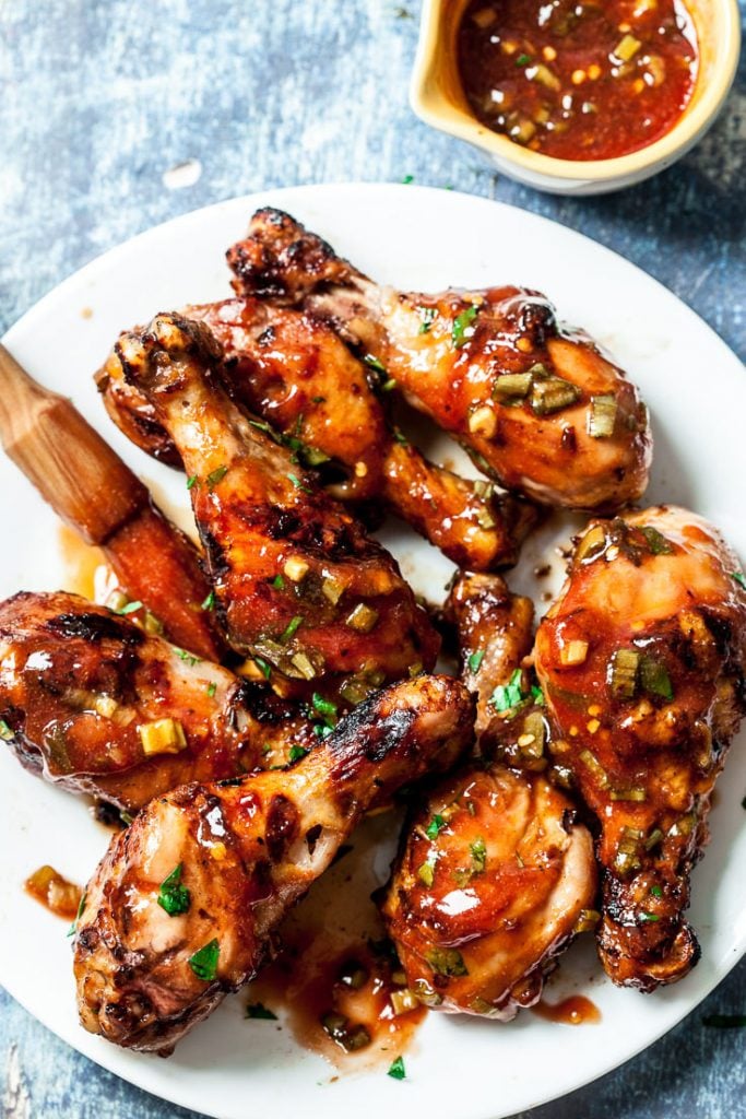 Grilled asian inspired chicken legs cooked and laid out on a plate next to a plate of extra barbecue sauce.