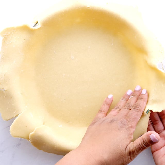 A hand pressing pie dough into a pie pan to make sweet cherry pie at home.