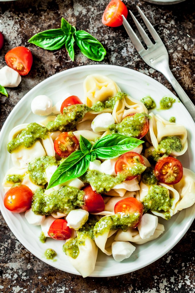 tortellini pasta salad with pesto sauce, mozzarella, and tomatoes on a plate