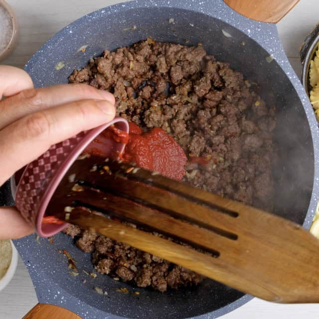 Tomato paste being added to pot with browned sausage.