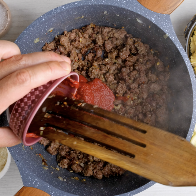 Tomato paste being added to pot with browned sausage.