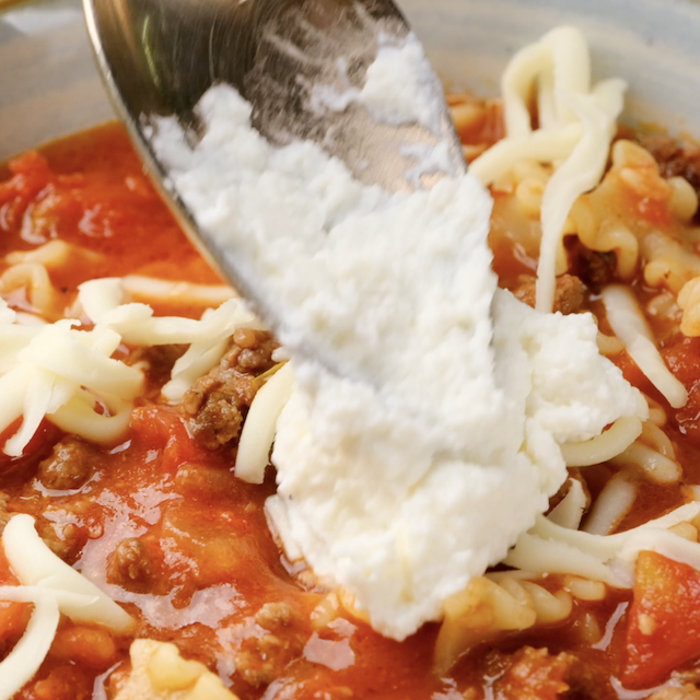 Ricotta cheese being added on top of lasagna soup.