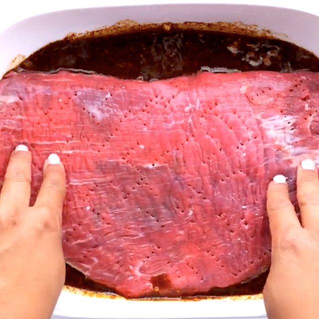 A big chunk of beef with holes poked into it in a dish with marinade to make carne asada tacos.