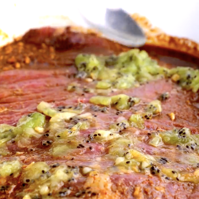 Mashed kiwi being spread over marinated skirt steak to make carne asada tacos.