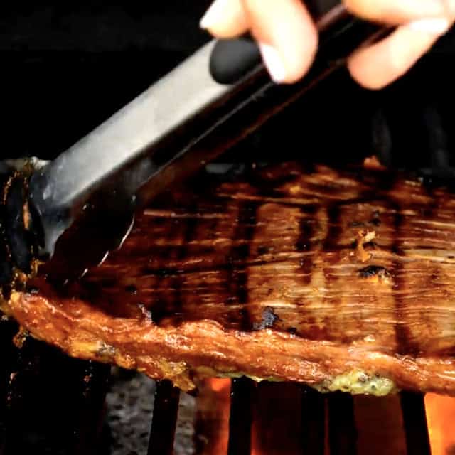 Skirt steak being grilled on both sides on an outside grill to make carne asada tacos.