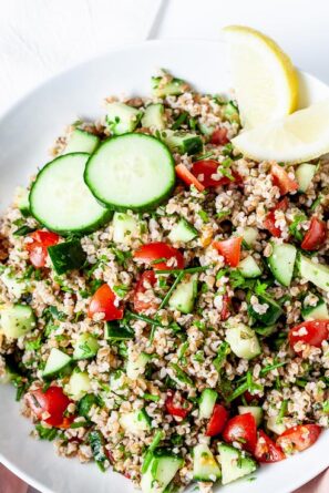 A plate of Tabbouleh with sliced of lemon and cucumber