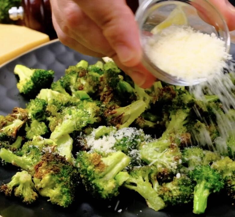 Air Fryer Broccoli being garnished with parmesan cheese and lemon.