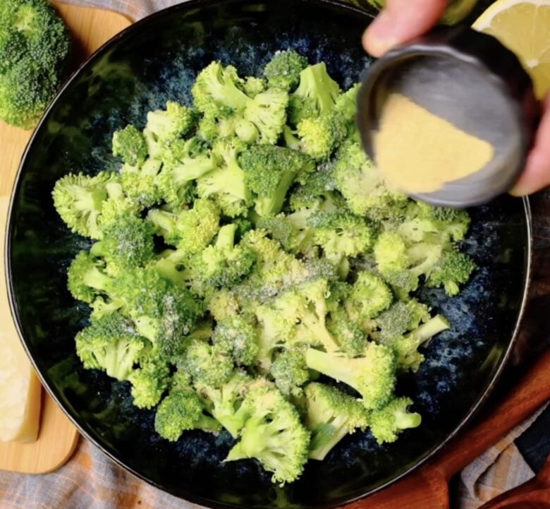 Air Fryer Broccoli being seasoned with garlic, onion, salt, and pepper.