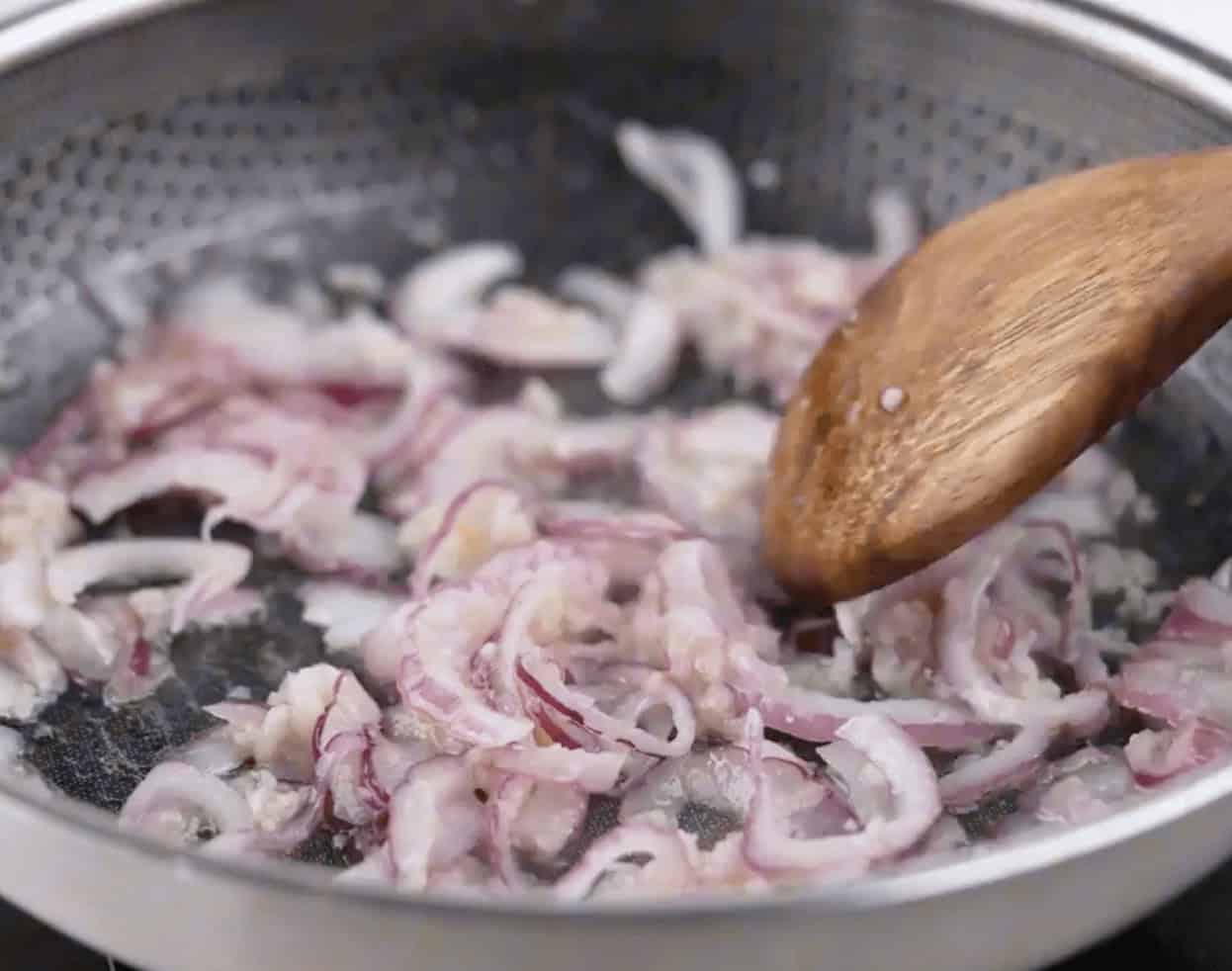 Cooking the onions in the skillet and stirring with a wooden spoon.