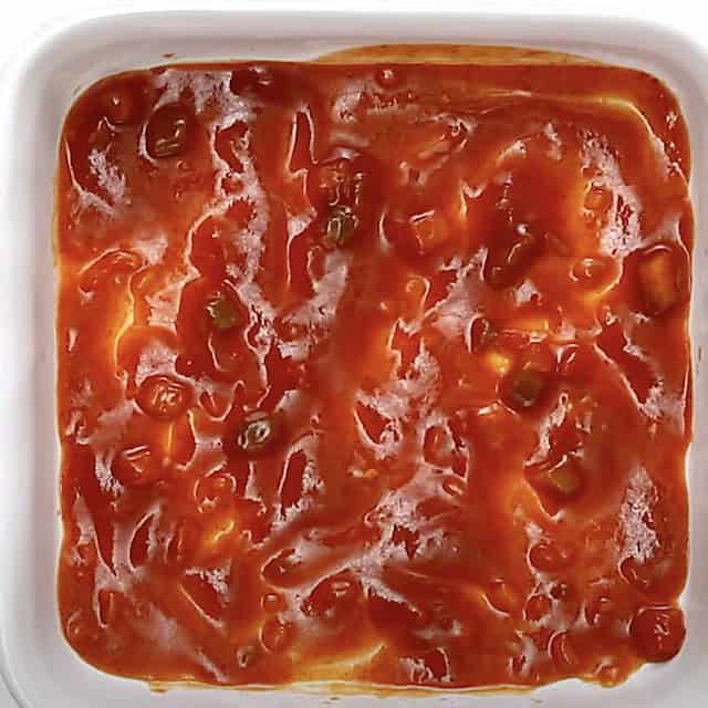 Enchilada sauce mixed with fire-roasted tomatoes in a baking dish to make Mexican Breakfast Casserole.