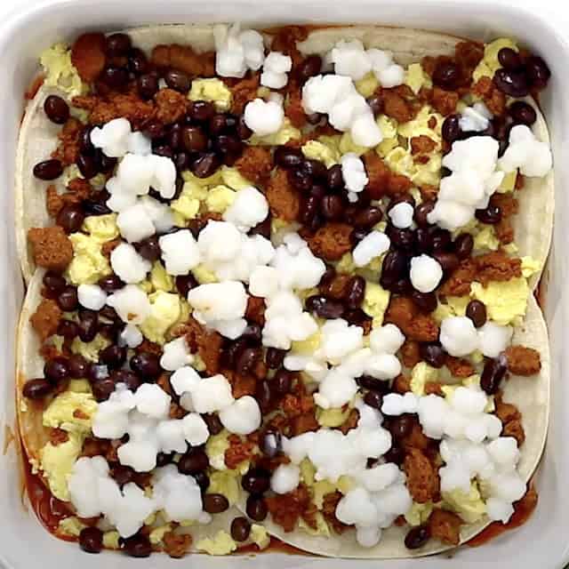 Layers of tortilla, eggs, chorizo, beans, cheese, and hominy in a baking dish to make Mexican breakfast casserole.