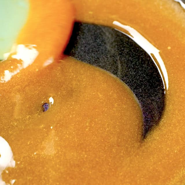 Honey glaze sauce being heated in a saucepan until thickened.