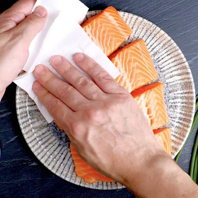 Salmon fillets being patted dry using paper towels.