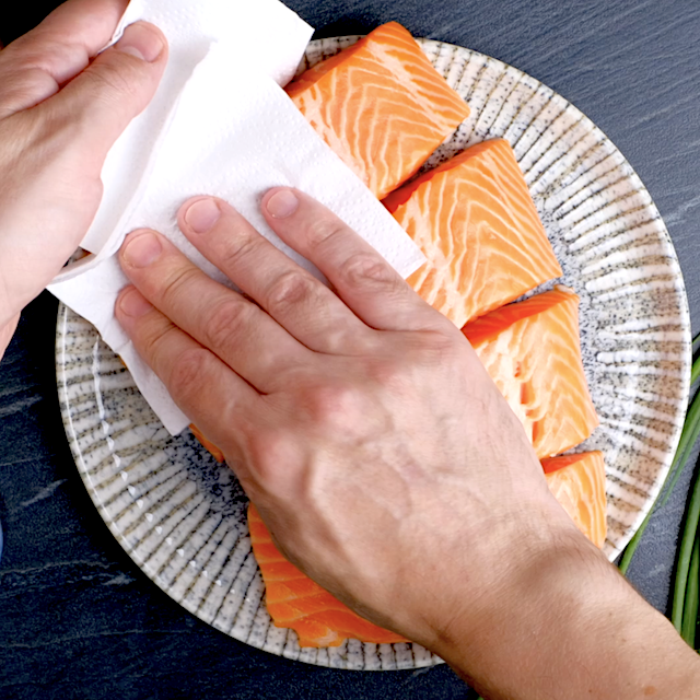 Salmon fillets being patted dry using paper towels.