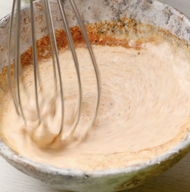 Dressing for Mexican street corn salad being mixed in a bowl with a whisk.