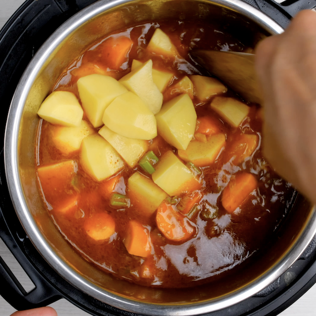 Vegetables being added to instant pot to make roast beef at home.