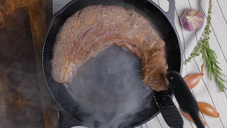 Beef tenderloin being seared in a pan.