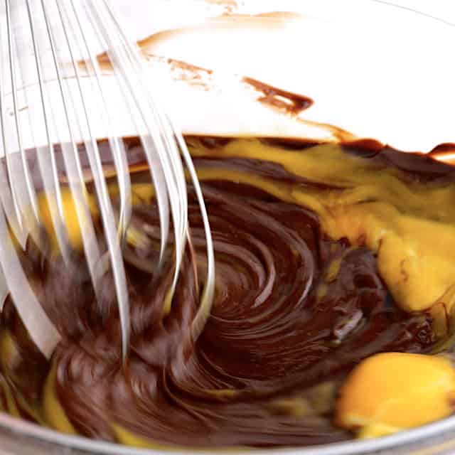 Egg yolks being mixed into chocolate mixture to make triple chocolate mousse cake.
