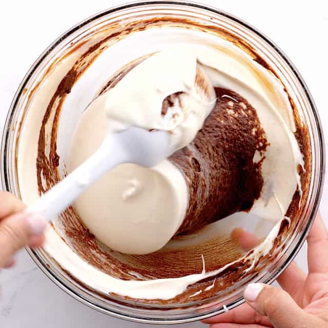 Chocolate mixture being folded into whipped egg white mixture to make triple chocolate mousse cake bottom layer.