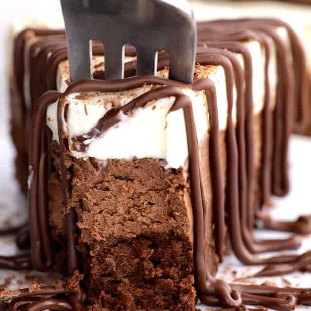 A fork being inserted into a slice of triple chocolate mousse cake.
