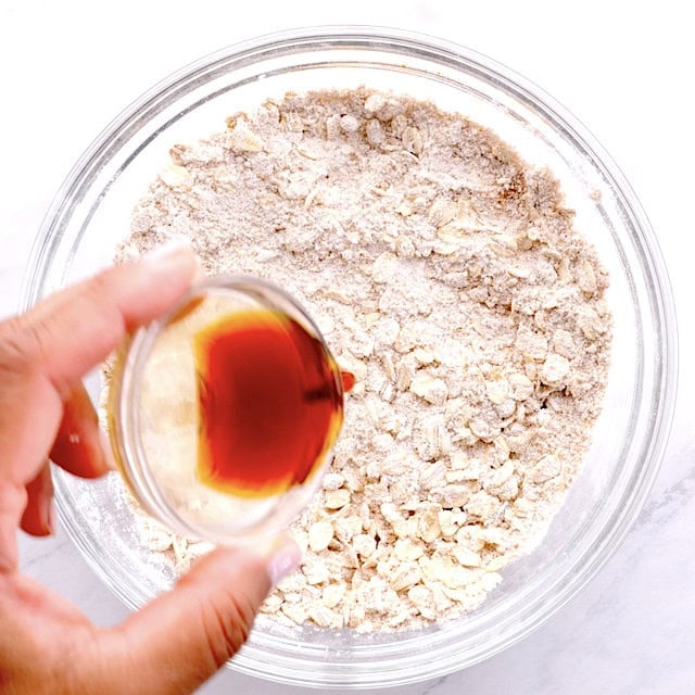 Vanilla extract being poured into a bowl with dry ingredients to make peach crisp.