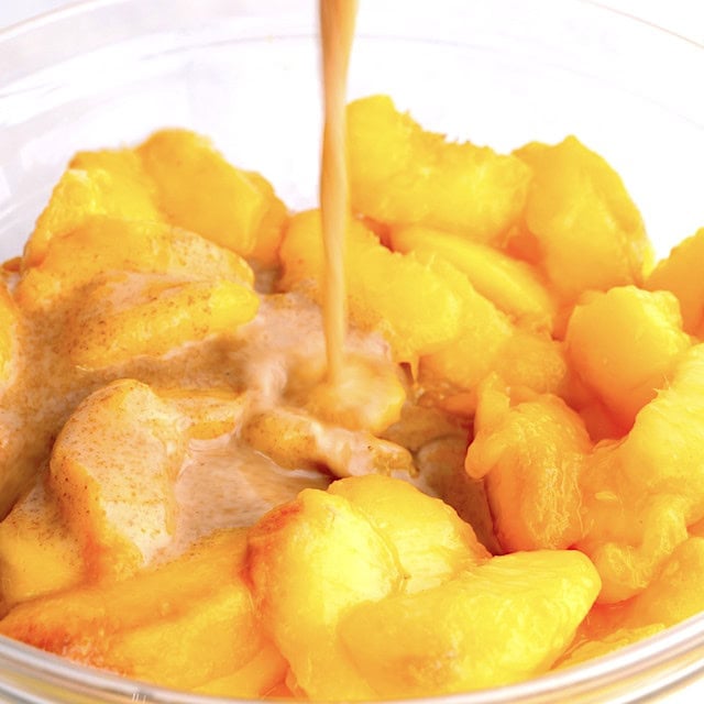 Lemon juice and spices mixture being poured over macerated peached to make peach crisp.