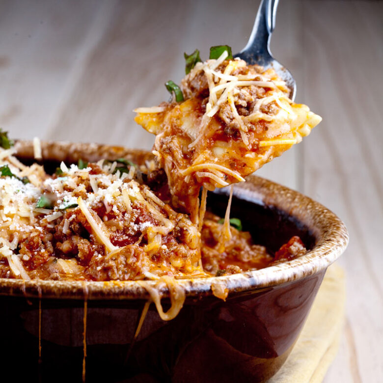 cheesy ravioli casserole in serving dish with spoon