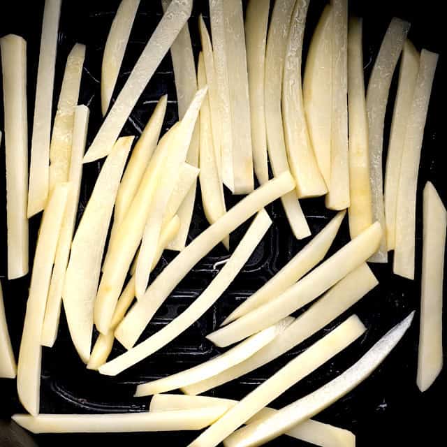 Evenly sliced potato strips in a single layer in the basket of an air fryer.