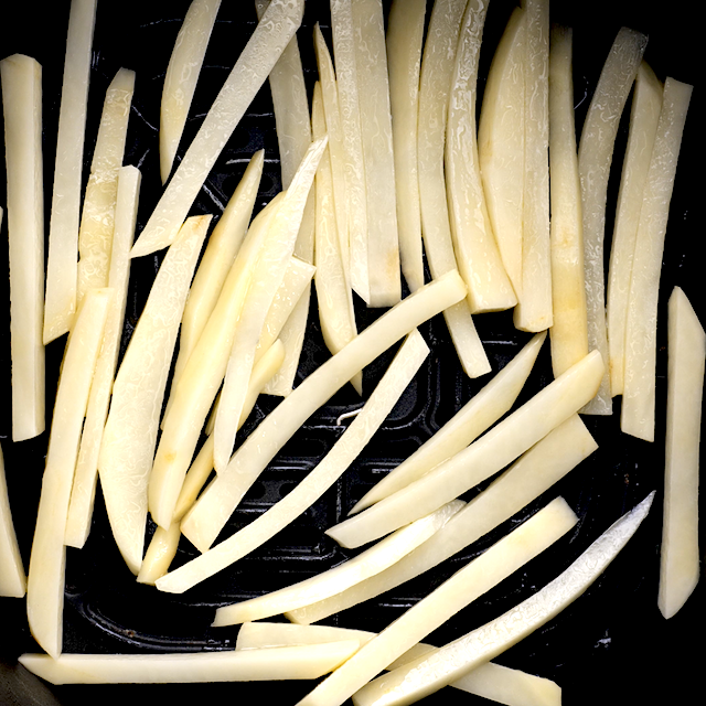 Evenly sliced potato strips in a single layer in the basket of an air fryer.
