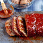 sliced juicy meatloaf on a pan slathered in sauce