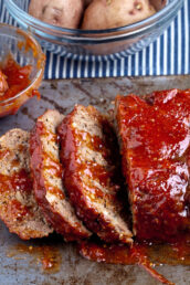 sliced juicy meatloaf on a pan slathered in sauce