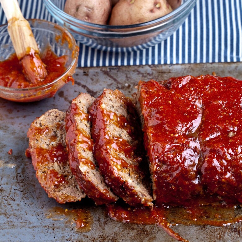 Sliced juicy meatloaf slathered in sauce on a pan.