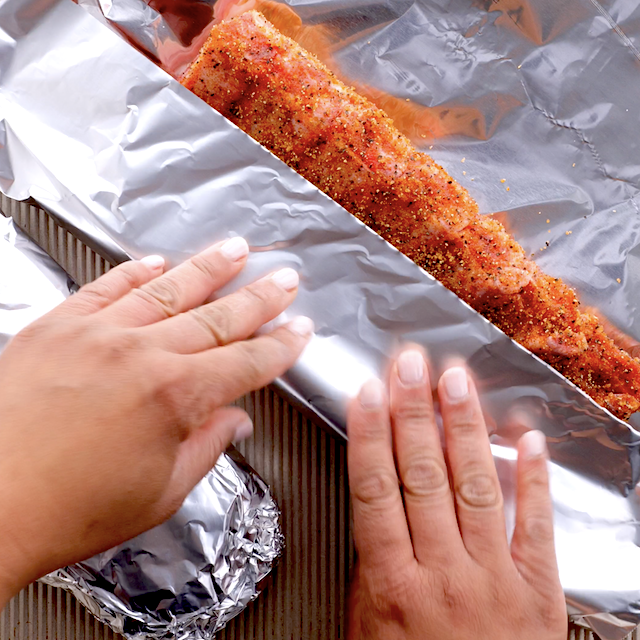 Rack of ribs being tightly wrapped in foil.